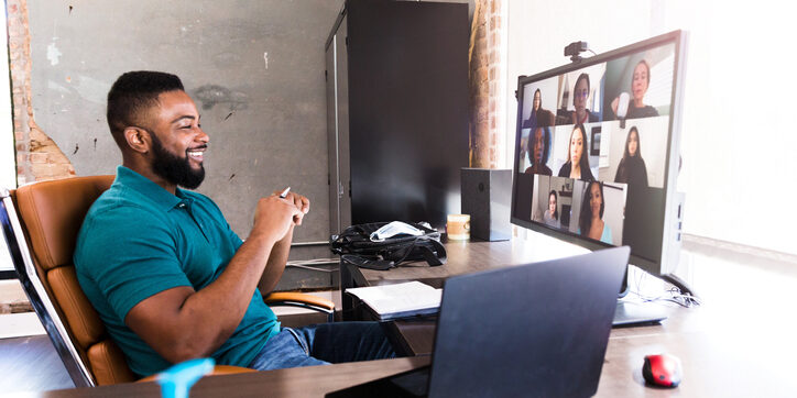 A mid adult businessman smiles confidently as he talks with a team of associates during a virtual meeting during the COVID-19 pandemic.